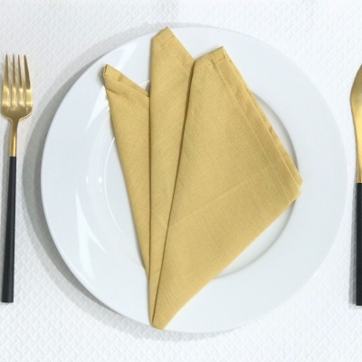 Conjunto de talheres dourados com cabos pretos e toalhete amarelo num prato branco sobre toalha branca texturizada