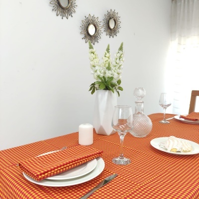 Mesa posta com toalha xadrez laranja e amarelo e decoração com flores e espelhos