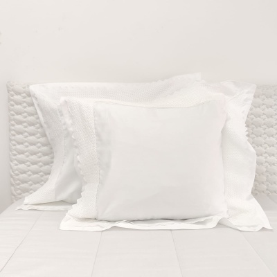 Três almofadas brancas sobre cama branca com cabeceira texturizada branca