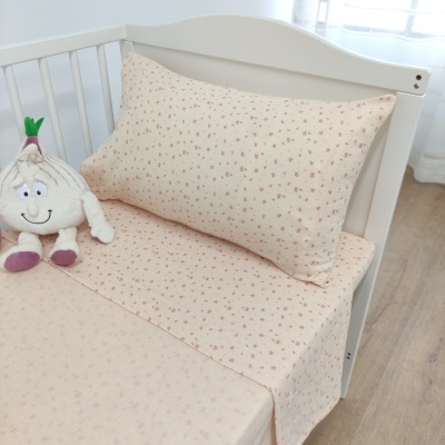 Cama de criança com roupa de cama creme e flores rosa e peluche de alho