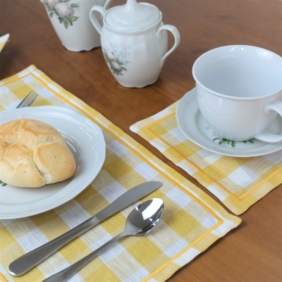 Mesa posta com toalhas xadrez amarelas e brancas, pratos, talheres, pão e utensílios de porcelana