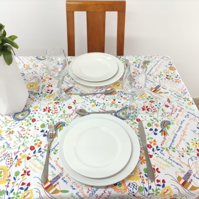 Mesa posta para duas pessoas com toalha de mesa colorida, loiça branca e copos de vidro