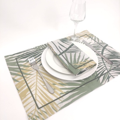 Jogo americano com padrão de folhas verdes e amarelas, prato branco, copo e talheres