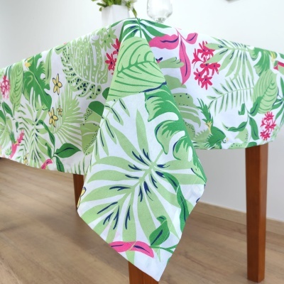 Toalha de mesa tropical com folhas verdes e flores cor-de-rosa sobre mesa de madeira