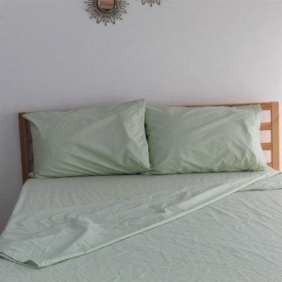 Cama de madeira com lençóis verdes e almofadas, parede branca e espelhos decorativos