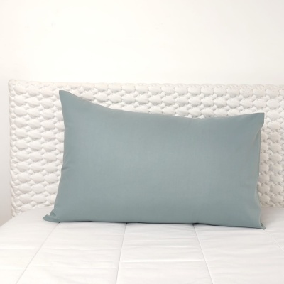 Almofada azul claro sobre cama com colchão e cabeceira branca estofada