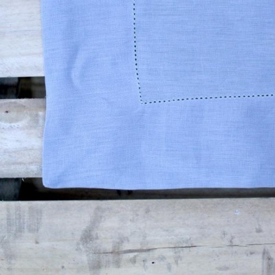 Toalha de mesa azul clara com bordado simples sobre superfície de madeira clara