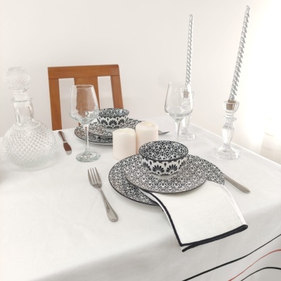 Mesa posta com conjunto de pratos e bowl com padrão floral preto e branco, talheres, copos de vidro e velas.