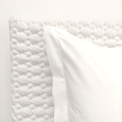 Almofada branca lisa sobre tecido branco acolchoado com padrão circular