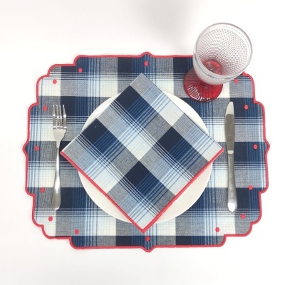 Conjunto de mesa com placemat e guardanapo xadrez azul e branco, talheres metálicos, prato branco e copo vermelho transparente