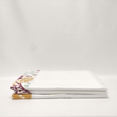 Jogo de cama branco com bordas estampadas coloridas dobrado sobre fundo branco