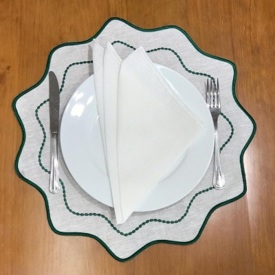 Conjunto de mesa com prato branco, guardanapo branco e talheres sobre passadeira de tecido branco bordado a verde