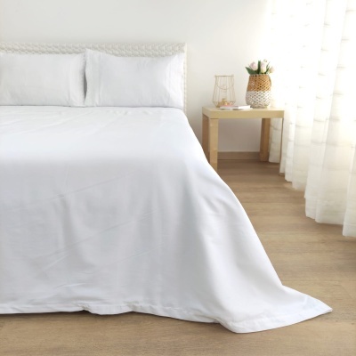 Cama branca com lençol, cabeceira texturizada, mesa de cabeceira com vaso e cortinas