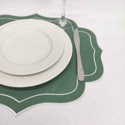 Aparelho de jantar com pratos brancos sobre individual verde decorativo e talher de metal