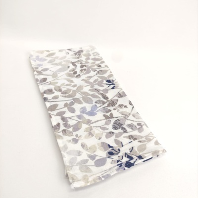 Pano de cozinha branco com padrão de folhas cinza, azul e bege sobre fundo branco