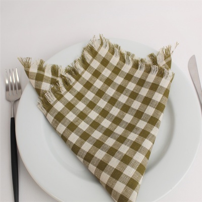 Guardanapo xadrez verde e branco no centro de prato branco, com talheres ao lado.