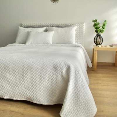 Cama com roupa de cama branca matelassada e mesa de madeira com vaso e planta