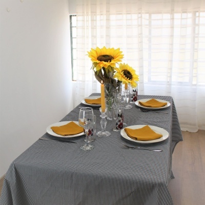 Mesa de jantar com toalha xadrez preta e branca, pratos brancos, guardanapos amarelos, copos decorados, castiçais com velas amarelas e vasos com girassóis.