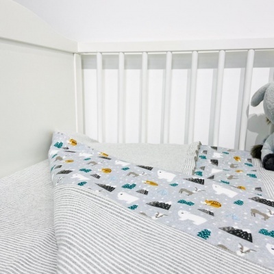 Berço branco com roupa de cama cinza, branco e cobertor com padrão de ursos e árvores