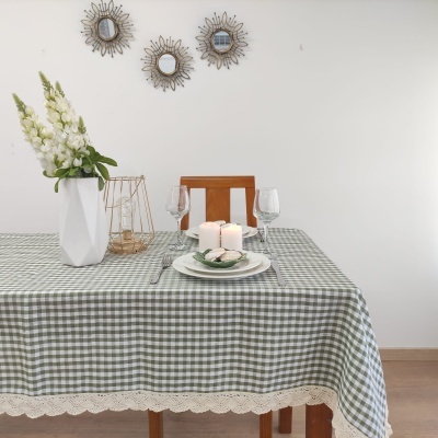 Mesa decorada com toalha xadrez verde e branca, flores brancas em vaso e velas, com três espelhos decorativos na parede branca