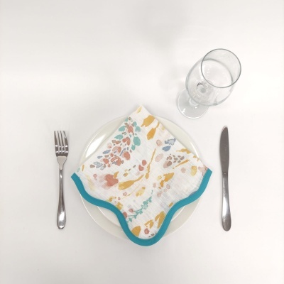 Prato branco com guardanapo floral e talheres dispostos sobre mesa branca