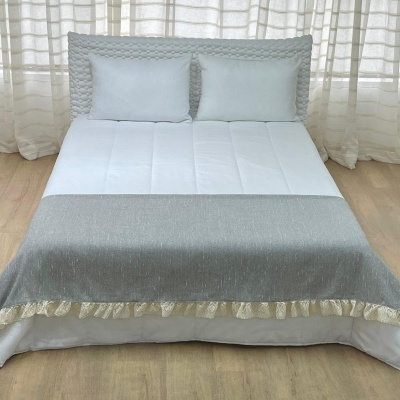 Cama de casal com colcha cinza e barra branca rendada, almofadas brancas e cortinas translúcidas