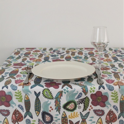 Mesa com toalha estampada com peixes e flores, prato branco, talheres e copo de vidro