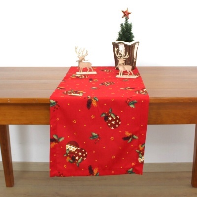 Toalha de mesa vermelha com padrão natalício e decorações de Natal numa mesa de madeira