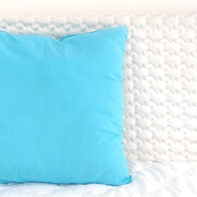 Almofada azul clara sobre cama com edredão branco e almofada com padrão trançado