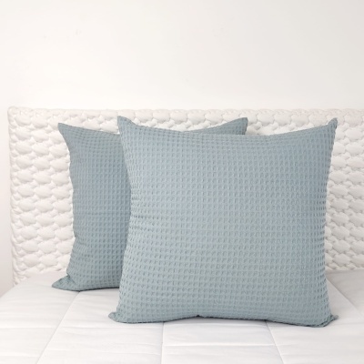 Duas almofadas cinza-azulado com textura tipo colmeia numa cama branca