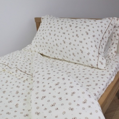 Conjunto de roupa de cama branca com padrão floral marron numa cama de madeira clara