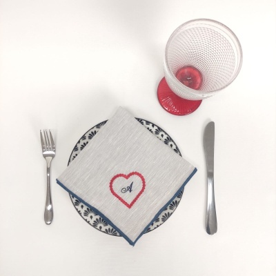 Lugar posto com talheres, prato azul e branco, guardanapo com bordado e copo transparente com base vermelha