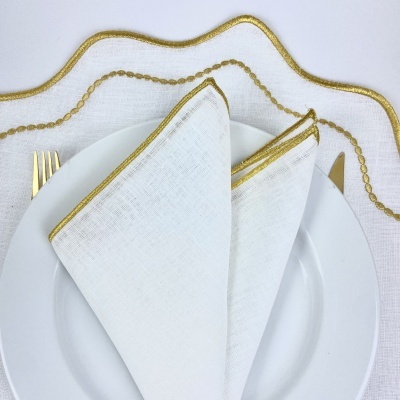 Conjunto de mesa com toalha branca e bordados dourados, guardanapo branco com borda dourada, prato e talheres dourados