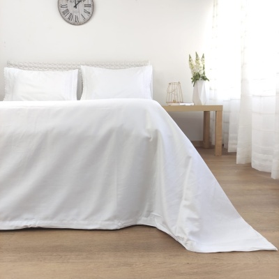 Cama com lençóis brancos e almofadas, mesa com vaso e flores, relógio na parede branca