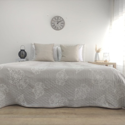 Cama com colcha cinza clara e almofadas claras numa decoração de quarto minimalista com relógio na parede