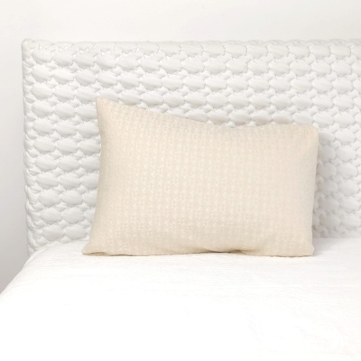 Almofada creme sobre cama branca com cabeceira estofada branca