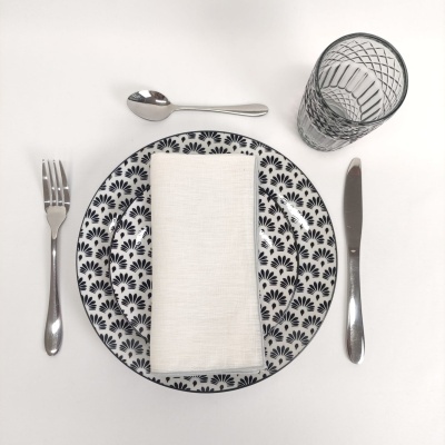 Conjunto de jantar com prato padrão preto e branco, guardanapo branco, talheres prateados e copo transparente com padrão geométrico