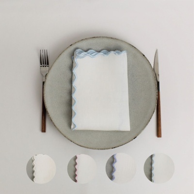 Guardanapo branco com borda azul claro sobre prato cinza e talheres com cabo de madeira