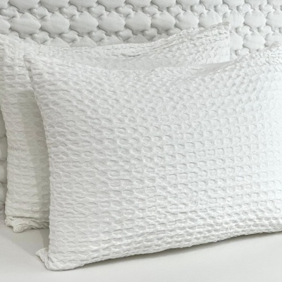Duas almofadas brancas texturizadas com padrão de colmeia em fundo branco.