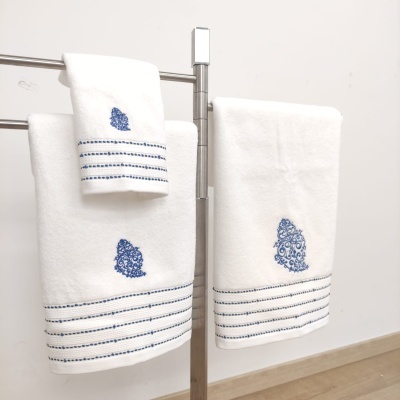 Toalhas brancas com bordados azuis penduradas em suporte metálico