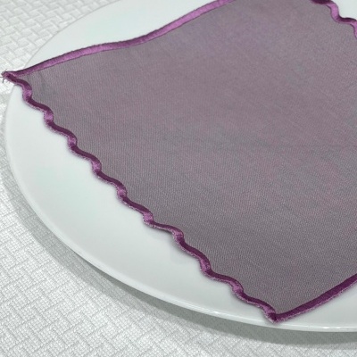 Guardanapo lavanda com borda ondulada roxa sobre prato branco e toalha texturizada