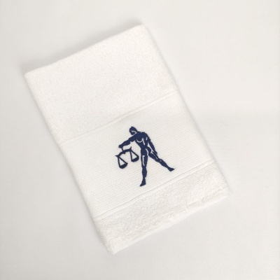 Toalha branca com bordado azul de figura humana segurando balança