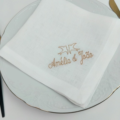 Guardanapo branco bordado sobre prato branco com borda dourada e talheres