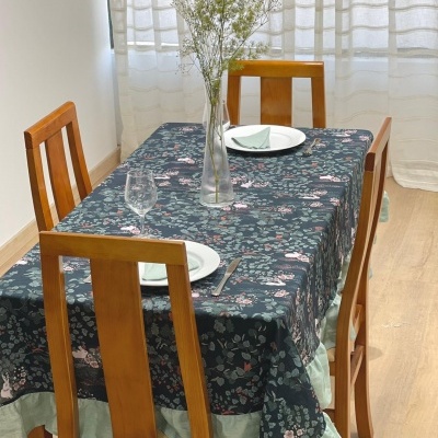 Mesa de jantar com toalha estampada escura, quatro cadeiras de madeira, pratos e copos, vaso com flores secas
