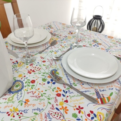 Mesa posta com toalha colorida de padrão floral e escrita, pratos brancos, copos de vinho e talheres