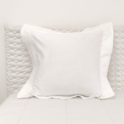 Travesseiro quadrado branco com capa bordada sobre cama branca com cabeceira acolchoada