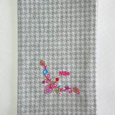 Toalha cinza com padrão pied-de-poule e bordado floral colorido com a palavra 'Mãe'