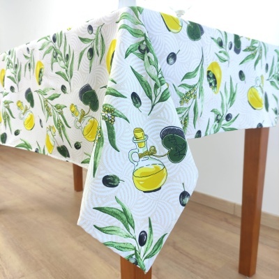 Toalha de mesa branca com padrão de oliveiras, azeitonas, limões e azeite sobre mesa de madeira.