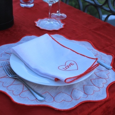 Conjunto de mesa com toalha vermelha, prato branco e guardanapo com padrão de corações e texto LOVE
