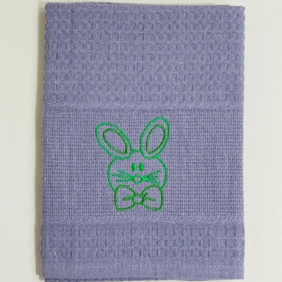 Toalha lilás com bordado verde de coelho e textura quadriculada
